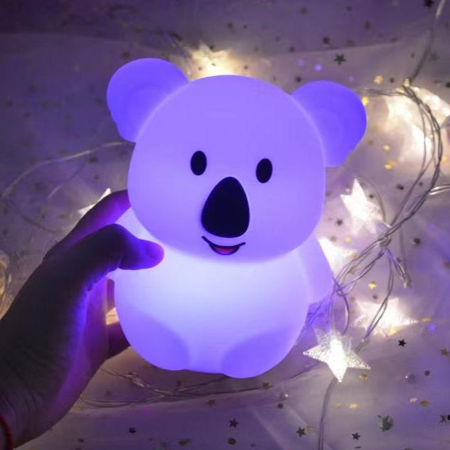 Hand holding a colorful koala-shaped night light with string lights in the background